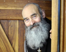 photo du père verlinde souriant devant une porte en bois de chêne.